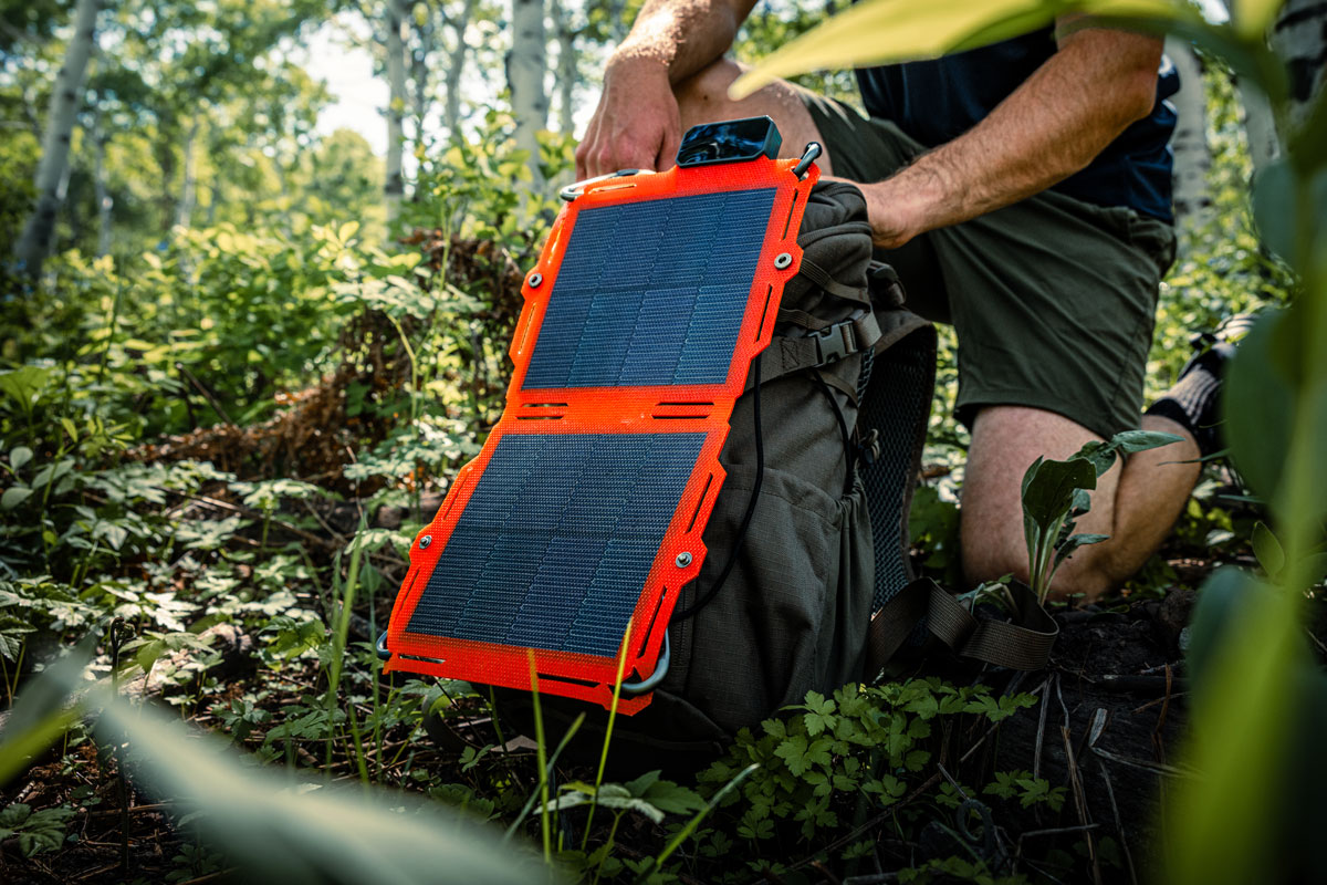 A hunter hiking through a rugged mountain canyon with a Dark Energy Spectre solar panel strapped to his backpack, charging his gear on the move.
