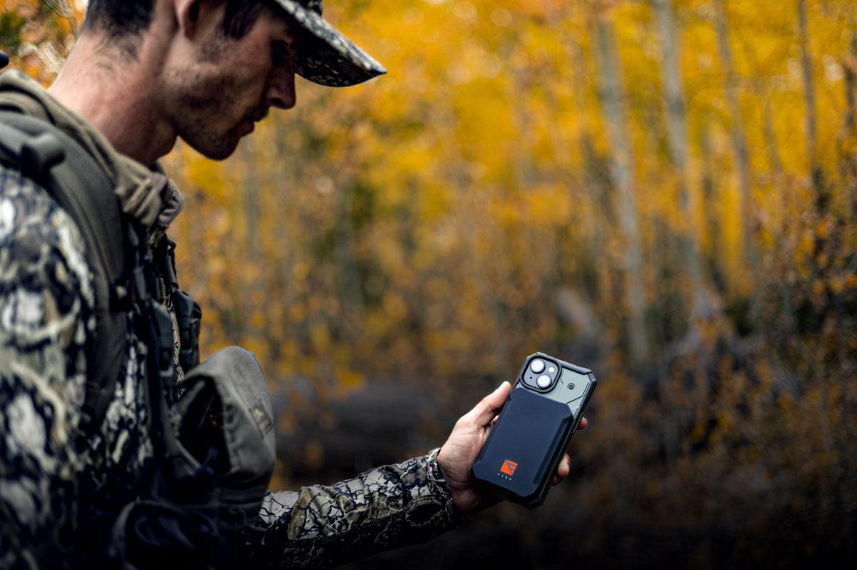A hunter in the backcountry checking his phone, which is protected and powered by a rugged Dark Energy Poseidon battery case.
