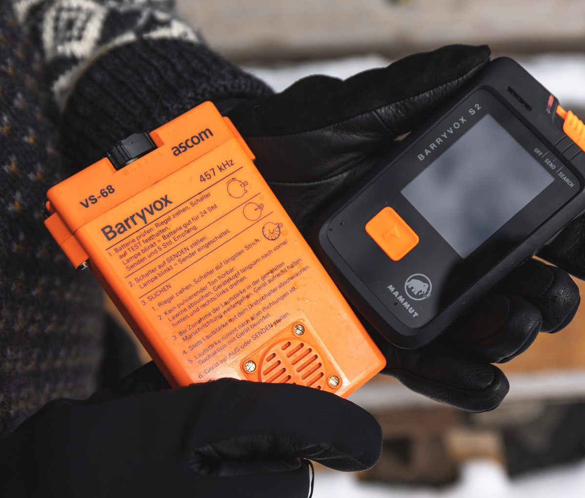 A side-by-side comparison showing the new, compact Mammut Barryvox S2 held next to the vintage, orange Mammut Barryvox VS-68, illustrating the evolution of avalanche transceivers.