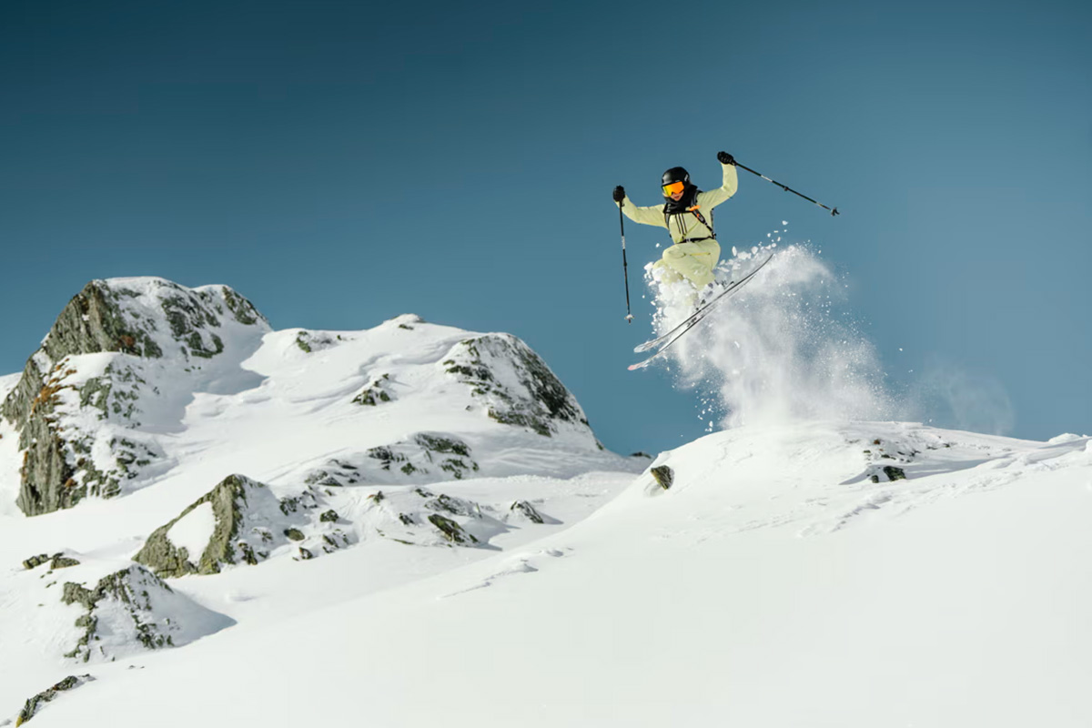 Skier wearing Mammut Haldigrat gear and carrying safety equipment through snowy backcountry terrain.